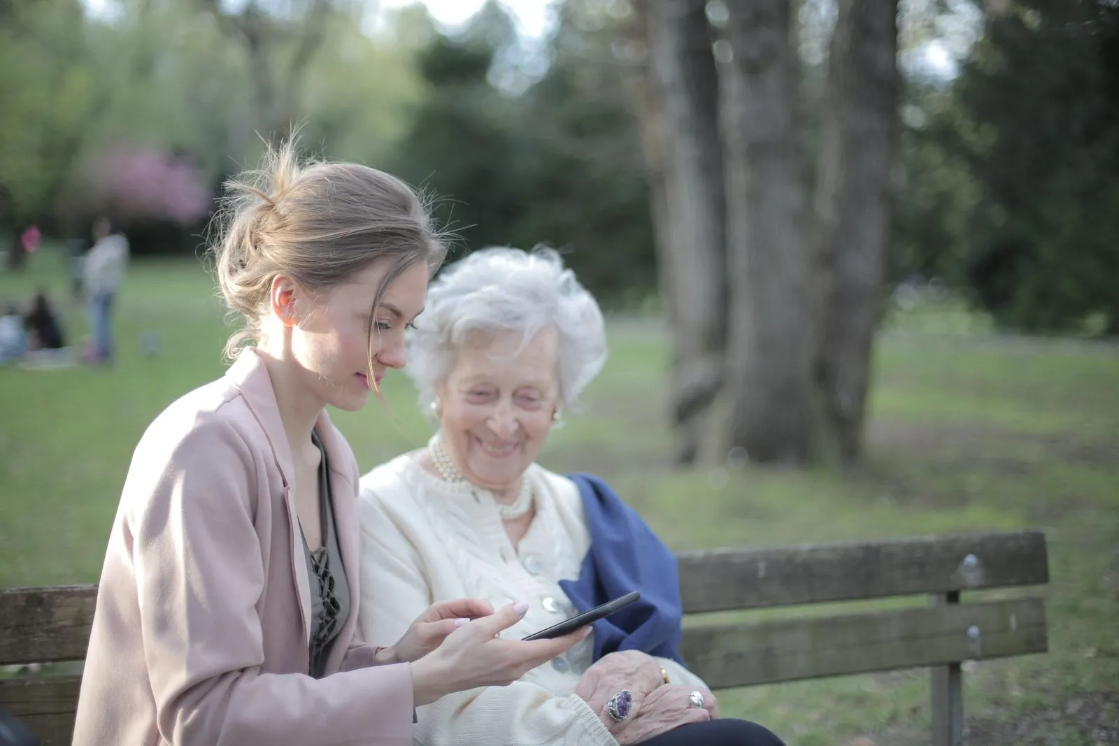 Caregiver and senior woman smiling together on a park bench