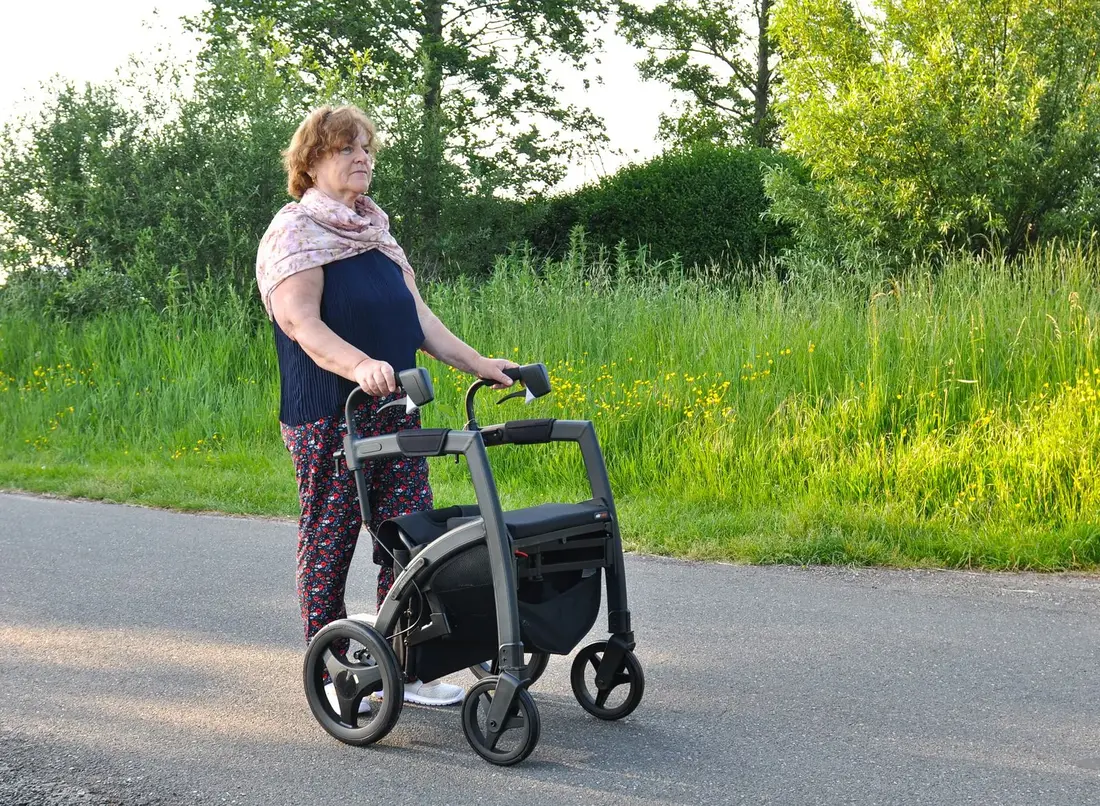 A senior woman walking outdoors with a rollator